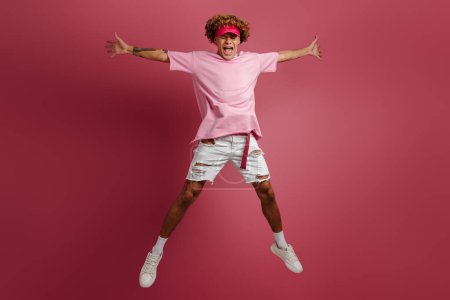 Téléchargez les photos : Pleine longueur de joyeux jeune homme à la mode sautant sur fond rouge - en image libre de droit