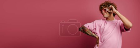 Téléchargez les photos : À la mode jeune bouclé cheveux gay homme dans rétro style lunettes regardant loin sur fond rose - en image libre de droit