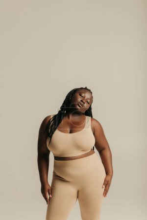 Foto de Mujer africana segura de talla grande en ropa interior que irradia amor propio mientras está de pie en el fondo del estudio - Imagen libre de derechos