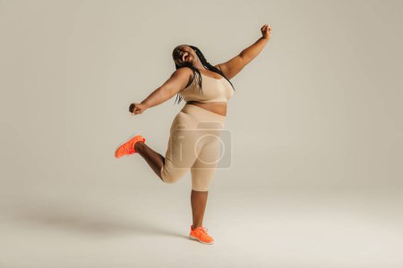 Téléchargez les photos : Pleine longueur heureux plus la taille femme africaine en vêtements de sport danse sur fond de studio - en image libre de droit
