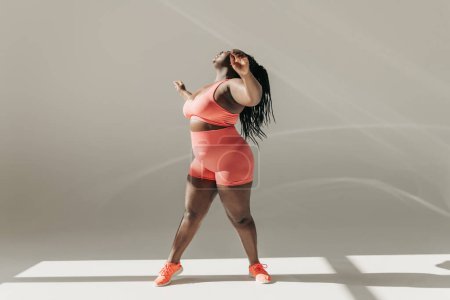 Foto de Longitud completa de la mujer africana activa más tamaño en ropa deportiva haciendo ejercicios de estiramiento en el gimnasio - Imagen libre de derechos