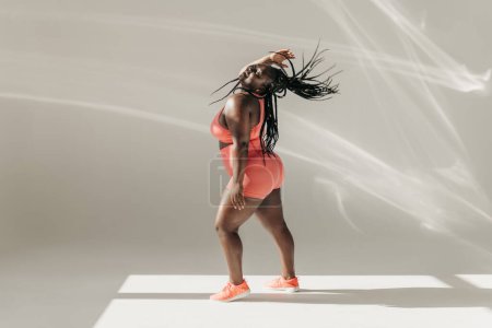Photo for Joyful African plus size woman in sportswear dancing and radiating self-love in fitness studio - Royalty Free Image