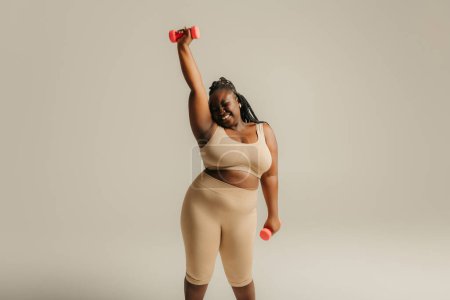 Téléchargez les photos : Confiant plus la taille de la femme africaine en vêtements de sport exercice avec haltères sur fond de studio - en image libre de droit