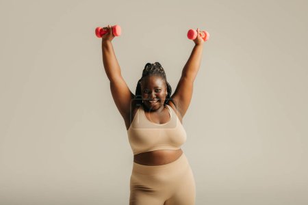 Téléchargez les photos : Belle femme africaine incurvée en tenue de sport rayonnant de confiance tout en faisant de l'exercice sur fond de studio - en image libre de droit