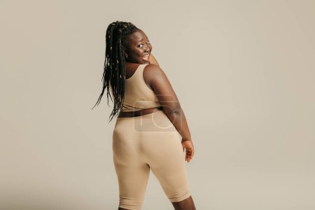 Foto de Vista trasera de la mujer africana con curvas felices en ropa deportiva mirando por encima del hombro en el fondo del estudio - Imagen libre de derechos