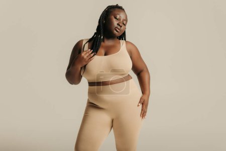 Foto de Atractiva mujer africana de talla grande en ropa interior que irradia amor propio mientras está de pie en el fondo del estudio - Imagen libre de derechos