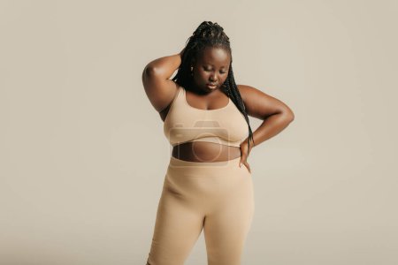 Foto de Hermosa mujer africana con curvas en ropa interior que mira confiado en su cuerpo en el fondo del estudio - Imagen libre de derechos