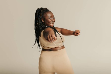 Téléchargez les photos : Vue arrière de la voluptueuse femme africaine en tenue de sport s'exerçant sur fond de studio - en image libre de droit