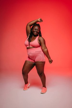 Photo for Happy African plus size woman in sportswear dancing and looking confident against vibrant background - Royalty Free Image