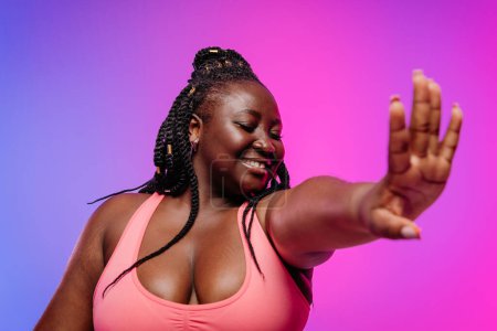 Photo for Beautiful African plus size woman in sportswear exercising and smiling on vibrant background - Royalty Free Image