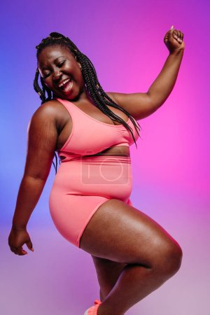 Photo for Happy plus size woman in sportswear dancing and smiling on colorful background - Royalty Free Image