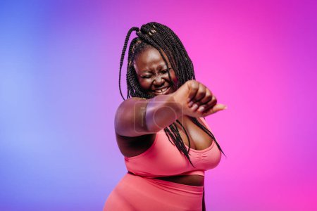 Téléchargez les photos : Belle femme courbée africaine en tenue de sport exerçant et souriant sur fond vibrant - en image libre de droit
