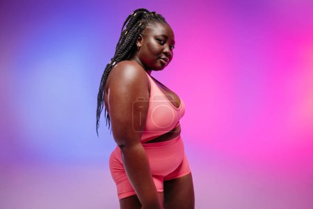 Photo for Beautiful African plus size woman in sportswear looking at camera while standing vibrant background - Royalty Free Image