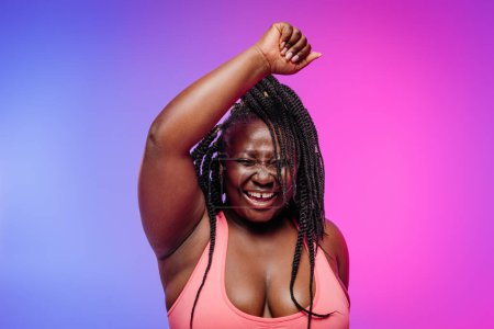 Photo for Joyful African plus size woman in sportswear exercising and smiling on vibrant background - Royalty Free Image