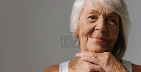 Téléchargez les photos : Portrait de femme souriante ealderly penché la tête sur les mains et souriant sur fond gris - en image libre de droit
