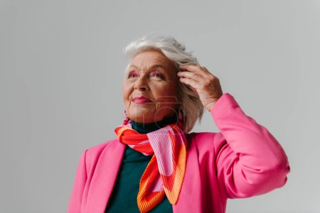 Téléchargez les photos : Femme âgée à la mode rayonnant de confiance et d'amour-propre tout en ajustant les cheveux gris sur fond - en image libre de droit