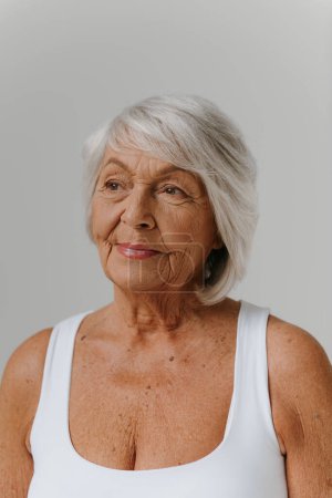 Foto de Retrato de mujer mayor de pelo gris confiado en camiseta sin mangas mirando hacia otro lado contra el fondo - Imagen libre de derechos