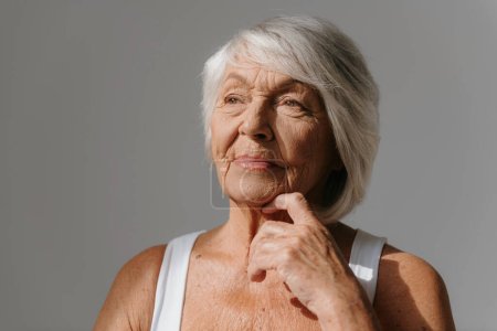 Téléchargez les photos : Portrait de femme âgée cheveux gris réfléchi en débardeur regardant loin sur fond - en image libre de droit
