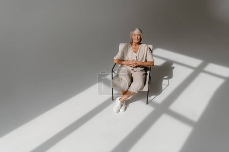 Foto de Vista superior de la mujer mayor de pelo gris calma relajante en silla cómoda en estudio soleado - Imagen libre de derechos