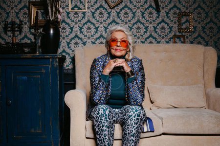 Foto de Elegante mujer de edad avanzada en ropa de lujo irradiando confianza y riqueza mientras se relaja en el hogar de estilo retro - Imagen libre de derechos