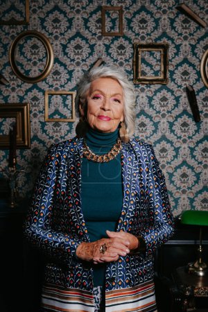 Téléchargez les photos : Femme âgée à la mode dans le luxe porter rayonnant de confiance tout en se tenant debout à l'intérieur de la maison de style rétro - en image libre de droit