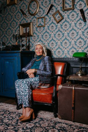 Foto de Mujer anciana de moda en el desgaste de lujo irradiando confianza y riqueza mientras se relaja en el hogar de estilo retro - Imagen libre de derechos