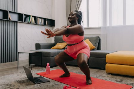 Téléchargez les photos : Happy plus taille femme africaine en vêtements de sport exercice à la maison - en image libre de droit