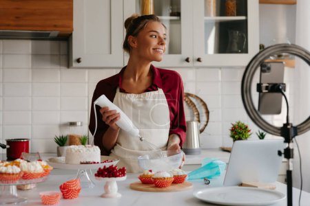 Foto de Cocinera de pastelería femenina segura batiendo una crema mientras hace un pastel en la cocina doméstica - Imagen libre de derechos