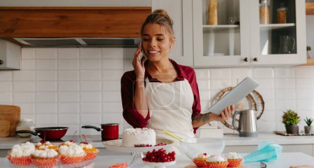Téléchargez les photos : Confiseur féminin confiant discutant des détails de la commande tout en parlant au téléphone avec le client à la cuisine - en image libre de droit