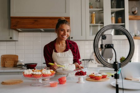 Photo for Confident young female pastry chef making a cake and streaming online from the domestic kitchen - Royalty Free Image