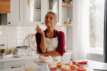 Téléchargez les photos : Joyeuse jeune pâtissière profitant de guimauve tout en décorant gâteau à la cuisine - en image libre de droit