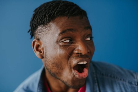 Photo for Portrait of surprised young African man in casual wear looking away on blue background - Royalty Free Image