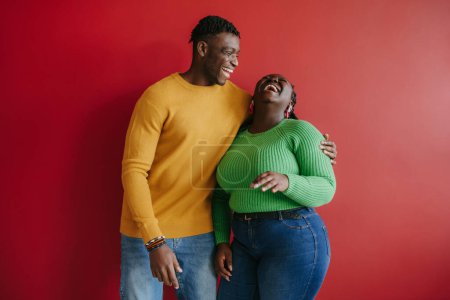 Photo for Beautiful young African couple embracing and laughing while standing on red background together - Royalty Free Image