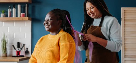 Téléchargez les photos : Heureux coiffeur afro-américain tressant les cheveux à une cliente dans le salon - en image libre de droit