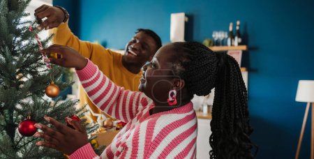 Téléchargez les photos : Beau jeune couple africain profiter du plaisir tout en décorant l'arbre de Noël à la maison ensemble - en image libre de droit