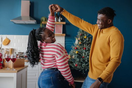 Foto de Feliz joven pareja africana bailando y sonriendo mientras celebran la Navidad en casa juntos - Imagen libre de derechos