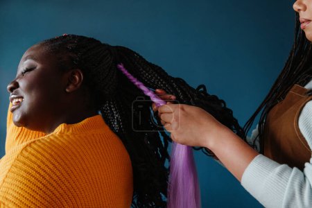 Téléchargez les photos : Gros plan du coiffeur tressant les cheveux d'une jeune Africaine souriante - en image libre de droit