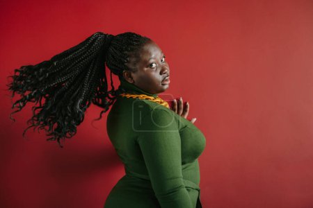 Foto de Hermosa mujer africana de talla grande con cabello trenzado mirando a la cámara sobre fondo rojo - Imagen libre de derechos