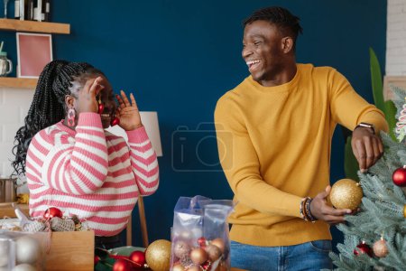 Téléchargez les photos : Beau jeune couple africain s'amuser tout en décorant l'arbre de Noël à la maison ensemble - en image libre de droit