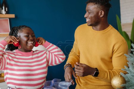 Photo for Joyful young African couple having fun while decorating Christmas tree at home together - Royalty Free Image