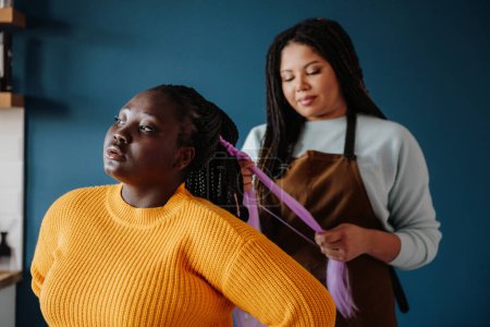 Photo for Confident African hairdresser braiding hair to a smiling female customer in salon - Royalty Free Image