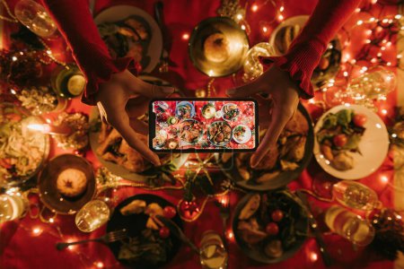 Photo for Close-up top view of woman photographing decorated Christmas table with variety of festive dishes - Royalty Free Image