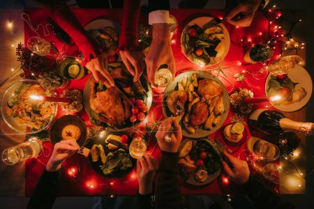 Photo for Top view of people enjoying variety of festive dishes while having Christmas dinner at the decorated table - Royalty Free Image