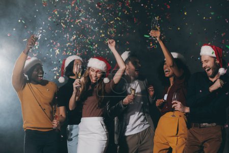 Téléchargez les photos : Groupe de jeunes gens heureux dansant et jetant des confettis tout en profitant de la fête du Nouvel An en boîte de nuit - en image libre de droit