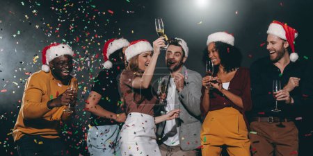 Photo for Happy young people in Christmas hats dancing and drinking champagne while celebrating New Year in night club - Royalty Free Image