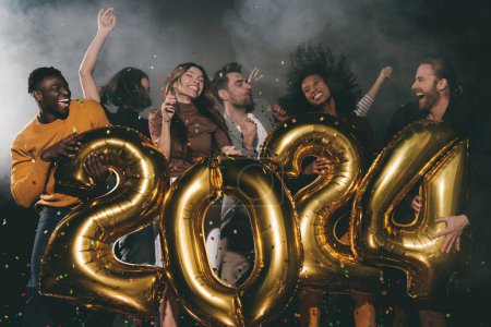 Foto de Grupo de jóvenes alegres celebrando el Año Nuevo 2024 mientras bailan y lanzan confeti en el club nocturno - Imagen libre de derechos