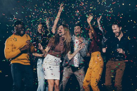 Foto de Grupo de jóvenes felices disfrutando del champán y lanzando confeti mientras bailan juntos en el club nocturno - Imagen libre de derechos