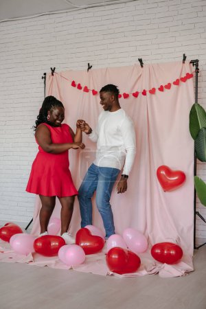Foto de Longitud completa de pareja africana joven romántica bailando sobre fondo de tela rosa con globos en forma de corazón - Imagen libre de derechos
