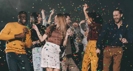 Photo for Group of joyful young people dancing and throwing confetti while enjoying party in the night club - Royalty Free Image