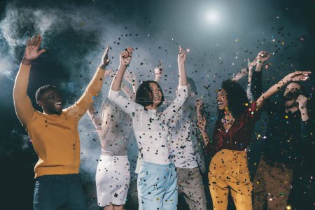 Foto de Grupo de jóvenes alegres bailando y lanzando confeti mientras se divierten en el club nocturno juntos - Imagen libre de derechos